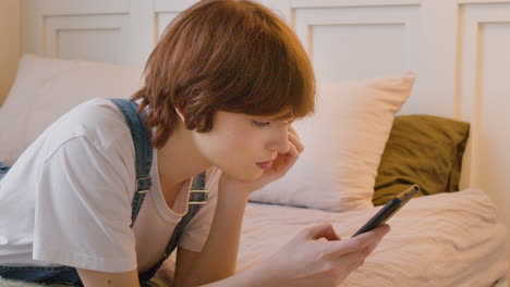 Side-View-Of-Girl-Lying-On-The-Bed-And-Using-Smartphone,-Tapping-And-Scrolling-On-The-Screen-2