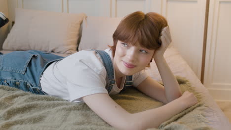 Girl-Lying-On-The-Bed-In-Bedroom-Smiling-And-Looking-At-Camera