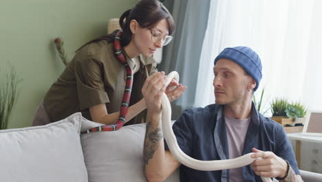 Couple-Holding-Pet-Snakes-And-Talking-Together-While-The-Man-Is-Sitting-And-Woman-Is-Leaning-On-A-Comfortable-Sofa-At-Home-2