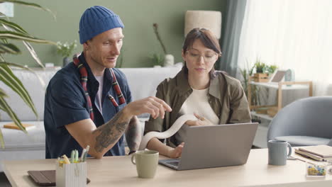 Couple-Holding-Pet-Snakes-Sitting-At-Desk-And-Using-Laptop