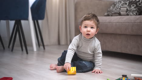 Baby-Spielt-Auf-Dem-Boden-Mit-Bauklötzen,-Steht-Dann-Auf-Und-Macht-Seine-Ersten-Schritte-Zur-Kamera