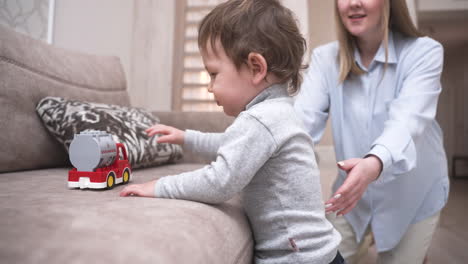 Baby-Taking-His-First-Steps-Near-The-Sofa-To-Take-A-Fire-Truck-Toy