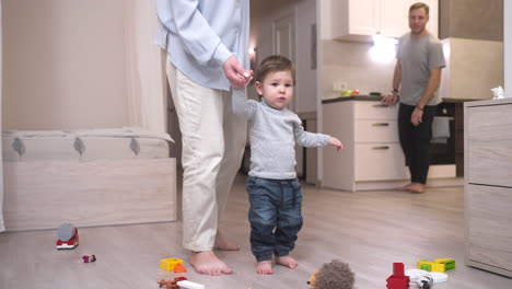 Mother-Helping-Her-Baby-To-Take-His-First-Steps-In-The-Living-Room-At-Home