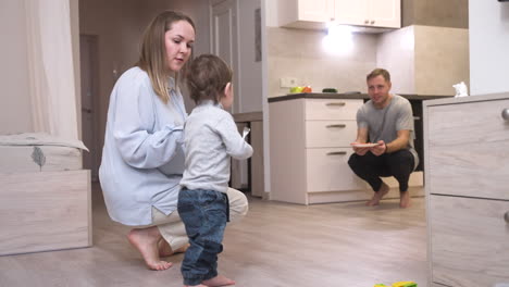 Mother-Helping-Her-Baby-To-Take-His-First-Steps-In-The-Living-Room-At-Home-1