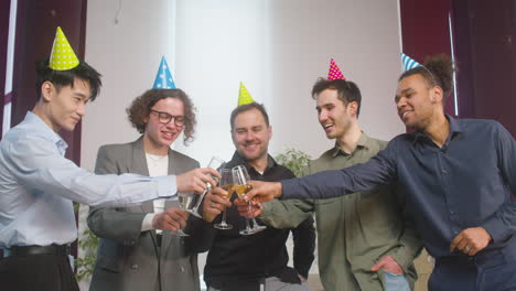 Happy-Multiethnic-Group-Of-Male-Colleagues-Toasting-Champagne-Glass-And-Then-Looking-At-The-Camera-At-The-Office-Party