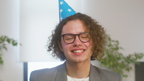 Portrait-Of-A-Happy-Curly-Boy-With-Party-Hat-Laughing-And-Looking-At-The-Camera-During-A-Office-Party