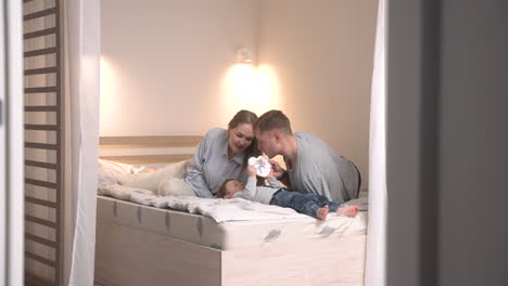 Distant-View-Of-Parents-Playing-With-Their-Child-In-Bed-While-The-Baby-Is-Holding-A-Toy-Heart