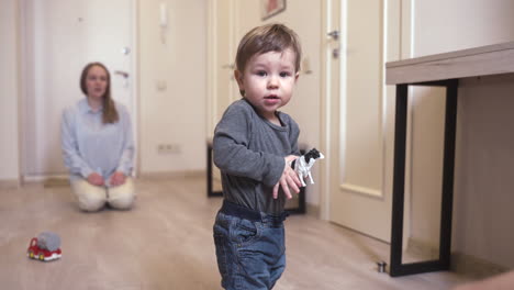 Baby-Schaut-In-Die-Kamera,-Während-Es-Ein-Spielzeug-Hält,-Das-Zu-Hause-Im-Korridor-Steht