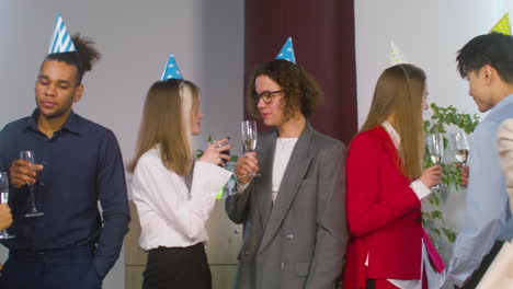 Group-Of-Multiethnic-Colleague-With-Party-Hat-Spending-Time-Together,-Drinking-And-Talking-At-The-Office-Party