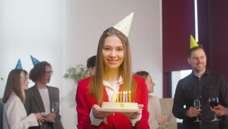 Portrait-Of-A-Beautiful-Woman-Holding-A-Birthday-Cake-And-Looking-At-Camera-During-A-Party-In-The-Office