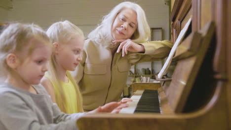Zwei-Kleine-Mädchen-Spielen-Zu-Hause-Altes-Klavier,-Während-Ihre-Großmutter-Sie-Beobachtet