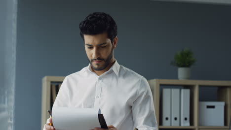 Handsome-Arabian-Businessman-In-White-Shirt-Standing-In-The-Office,-Flipping-Documents-Or-Contract,-Writing-And-Thinking-And-Looking-Out-The-Window