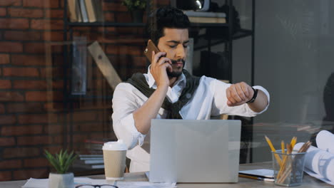 Stilvoller-Arabischer-Geschäftsmann,-Der-An-Seinem-Schreibtisch-Mit-Laptop-Im-Büro-Sitzt-Und-Telefoniert,-Dann-Aufsteht-Und-Weggeht
