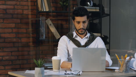 Gut-Aussehender-Arabischer-Geschäftsmann,-Der-Am-Tisch-Sitzt-Und-Am-Laptop-Arbeitet,-Trinkt-Dann-Kaffee