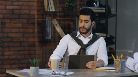 Gut-Aussehender-Arabischer-Geschäftsmann,-Der-Am-Schreibtisch-Sitzt-Und-Am-Tablet-Arbeitet,-Dann-Trinkt-Er-Kaffee