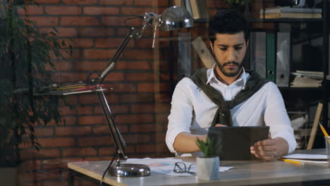 Good-Looking-Arabian-Businessman-Taping-And-Typing-On-The-Tablet-While-Sitting-At-Desk-In-The-Office