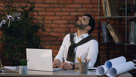 Cansado-Hombre-De-Negocios-árabe-Haciendo-Un-Ejercicio-Para-El-Cuello-Y-Descansando-Mientras-Está-Sentado-En-Su-Oficina-Trabajando-Con-Una-Laptop