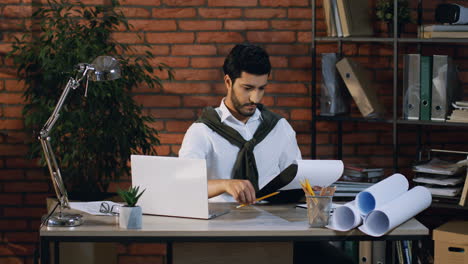 Junger-Arabischer-Geschäftsmann,-Der-Einige-Dokumente-Oder-Verträge-überprüft-Und-Liest,-Während-Er-Im-Büro-Am-Computer-Sitzt
