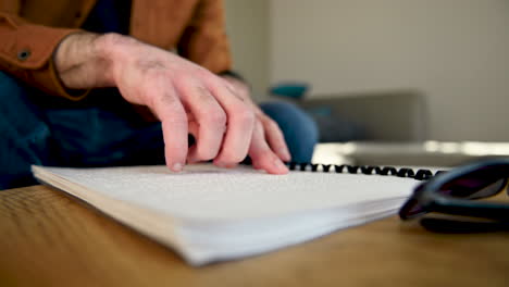 Close-Up-Of-An-Unrecognizable-Blind-Man-Reading-A-Braille-Book-While-Sitting-On-The-Sofa-At-Home-1