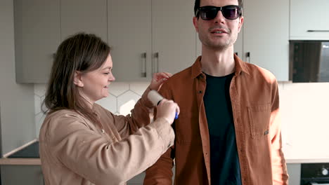 Smiling-Woman-Helping-A-Blind-Man-To-Clean-His-Clothes-With-Lint-Roller-While-Talking-Together-At-Home