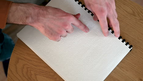 Vista-Superior-De-Un-Hombre-Irreconocible-Leyendo-Un-Libro-En-Braille-En-Casa