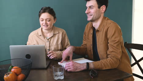 Smiling-Woman-With-Laptop-Computer-And-A-Blind-Man-With-Braille-Book-Talking-And-Drinking-Water-While-Sitting-At-Table-At-Home