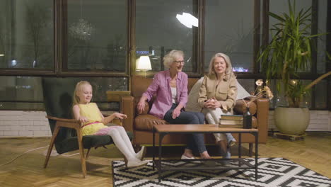 Kleines-Mädchen-Spielt-Im-Wohnzimmer,-Während-Ihre-Beiden-Großmütter-Auf-Dem-Sofa-Sitzen-Und-Sie-Beobachten