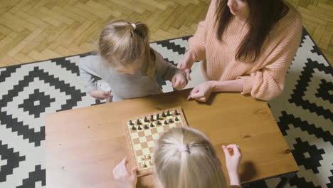 Top-View-Of-Mother-And-Her-Two-Little-Daughters-Playing-Chess-At-Home