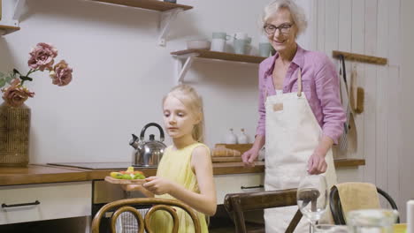 Kleines-Mädchen,-Das-Ihrer-Großmutter-Hilft,-Den-Tisch-Zum-Abendessen-Zu-Decken-Und-Ein-Tablett-Mit-Frischen-Lebensmitteln-Zu-Bringen
