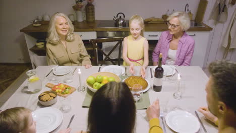 Kleines-Mädchen,-Das-Während-Eines-Abendessens-Mit-Ihrer-Glücklichen-Familie-Kuchen-Auf-Den-Tisch-Bringt