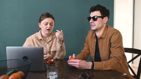 Woman-And-Blind-Man-With-Glasses-Peeling-And-Eating-Tangerines-While-Talking-Sitting-At-Table-At-Home