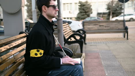 Blind-Man-With-Armband-Reading-A-Braille-Book-While-Sitting-On-Bench-Outdoors