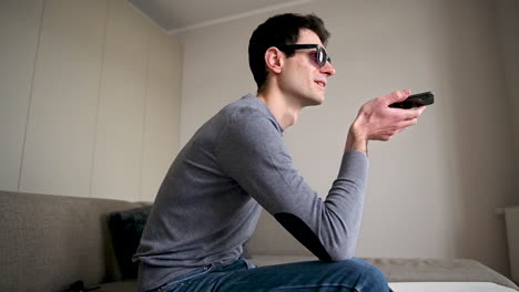 Side-View-Of-A-Blind-Man-In-Sunglasses-Sitting-On-The-Sofa-At-Home-While-Holding-A-Smartphone-And-Having-A-Hands-Free-Call