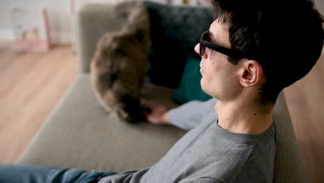 Seitenansicht-Eines-Blinden-Mannes-Mit-Sonnenbrille,-Der-Zu-Hause-Auf-Dem-Sofa-Sitzt-Und-Seine-Katze-Streichelt