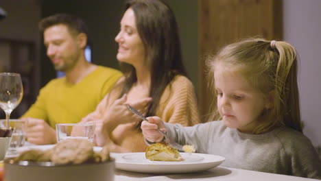 Side-View-Of-Blonde-Little-Girl-Eating-Apple-Pie-Sitting-At-The-Table-While-Her-Parents-Talking-During-Dinner