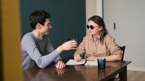 Man-And-Blind-Woman-In-Sunglasses-Sitting-At-Table-At-Home-Talking