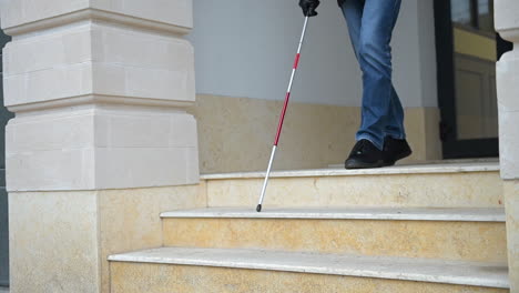 Side-View-Of-An-Unrecognizable-Blind-Man-Holding-A-Walking-Stick-And-Walking-Out-Of-A-Building-While-Going-Down-The-Stairs