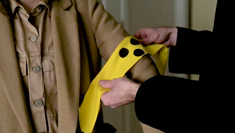 Man-Putting-An-Yellow-Armband-With-Three-Black-Points-On-A-Blind-Woman