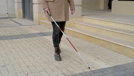 Mid-View-Of-A-Blind-Woman-In-Brown-Coat-Walking-With-A-Walking-Stick-In-The-Street