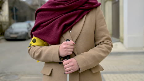 Vorderansicht-Einer-Nicht-Erkennbaren-Frau-In-Braunem-Mantel-Und-Schal,-Die-Einen-Spazierstock-Hält-Und-Eine-Gelbe-Armbinde-Trägt