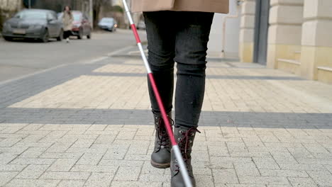 Mid-View-Of-A-Blind-Woman-In-Brown-Coat-And-Black-Boots-Walking-With-A-Walking-Stick-In-The-Street