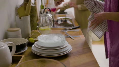 Side-View-Of-A-Mature-Woman's-Hands-Drying-The-Plates-And-Cutlery-For-A-Family-Dinner-In-The-Kitchen