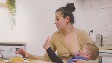 Young-Mother-Working-With-Laptop-Computer-And-Breastfeeding-Her-Baby-Boy-At-Home-2