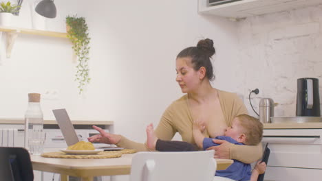 Young-Mother-Working-With-Laptop-Computer-And-Breastfeeding-Her-Baby-Boy-At-Home-3
