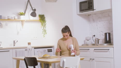 Young-Mother-Using-Breast-Pump-While-Sitting-At-Table-At-Home