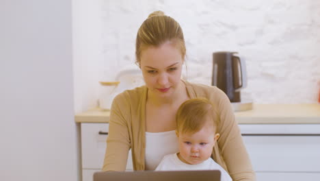 Portrait-Of-A-Young-Woman-Working-On-Laptop-Computer-While-Sitting-With-Baby-Boy-At-Home