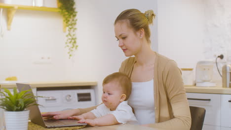 Mujer-Joven-Que-Trabaja-En-Una-Computadora-Portátil-Mientras-Se-Sienta-Con-Un-Bebé-En-Casa-3