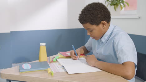Junge-Sitzt-Am-Schreibtisch-Und-Schreibt-Während-Des-Englischunterrichts-In-Der-Schule-In-Ein-Notizbuch-1