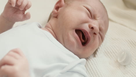 Close-Up-Of-A-Cute-Newborn-Baby-Lying-On-Bed,-Crying-And-Then-Calming-Down