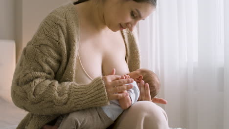 Loving-Young-Mother-Breastfeeding-Her-Newborn-Baby-While-Sitting-On-The-Bed-At-Home